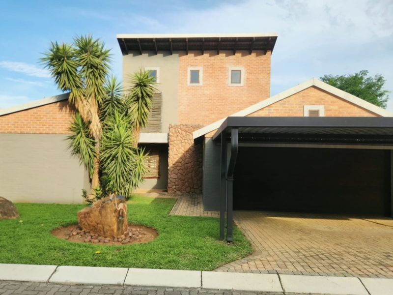 Front elevation of a modern house featuring a combination of brick and stone cladding, a paved driveway, and a covered carport.