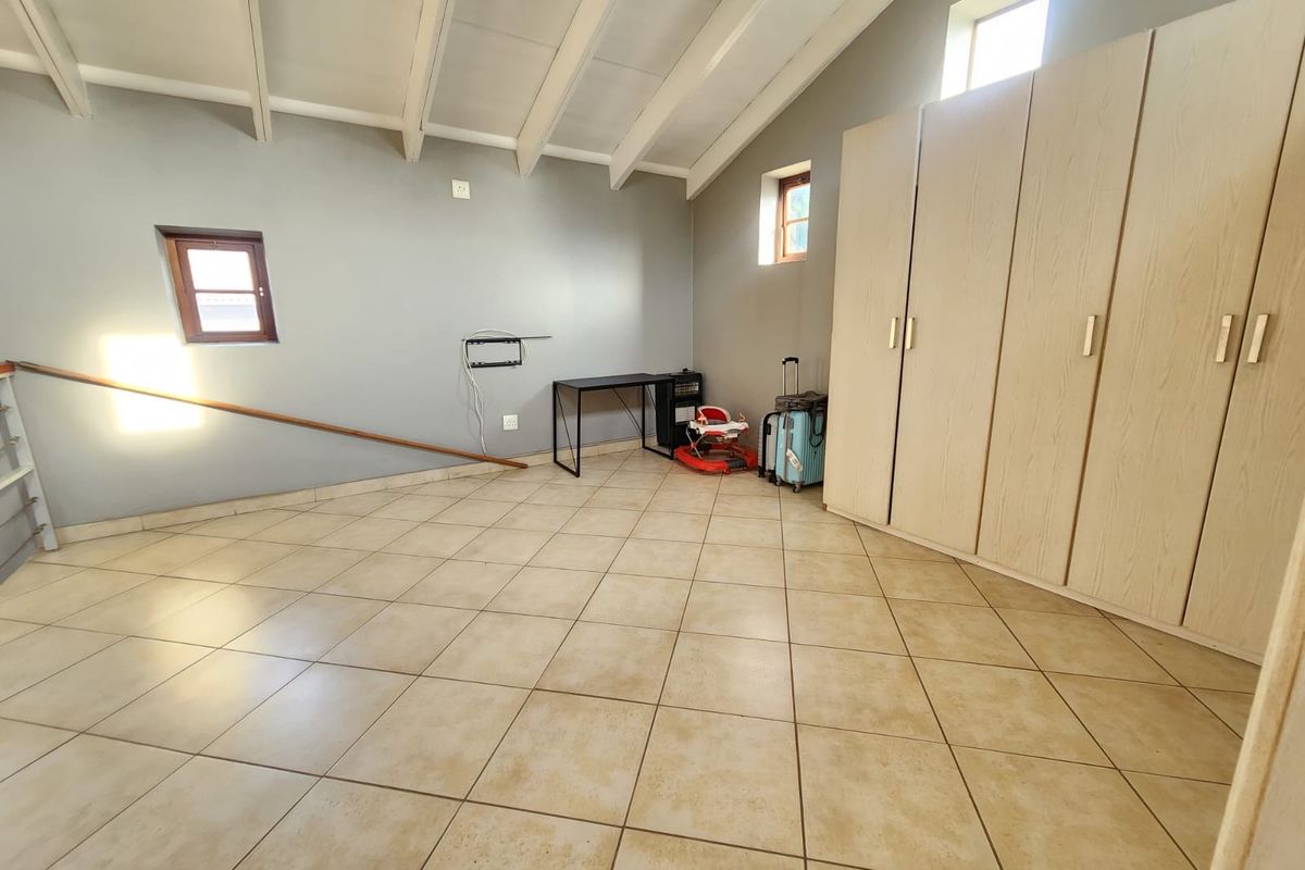 Spacious bedroom featuring high exposed beam ceilings, neutral tiled flooring, and extensive built-in cupboard storage.