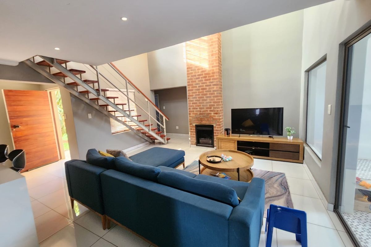 Spacious double-volume living room featuring an exposed brick fireplace, modern staircase, tiled flooring, and large sliding doors providing ample natural light.