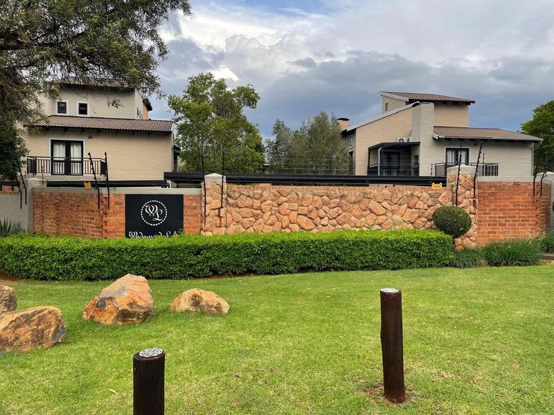 Front view of the property entrance featuring a decorative brick and stone boundary wall with integrated electric fencing and well-maintained garden landscaping.