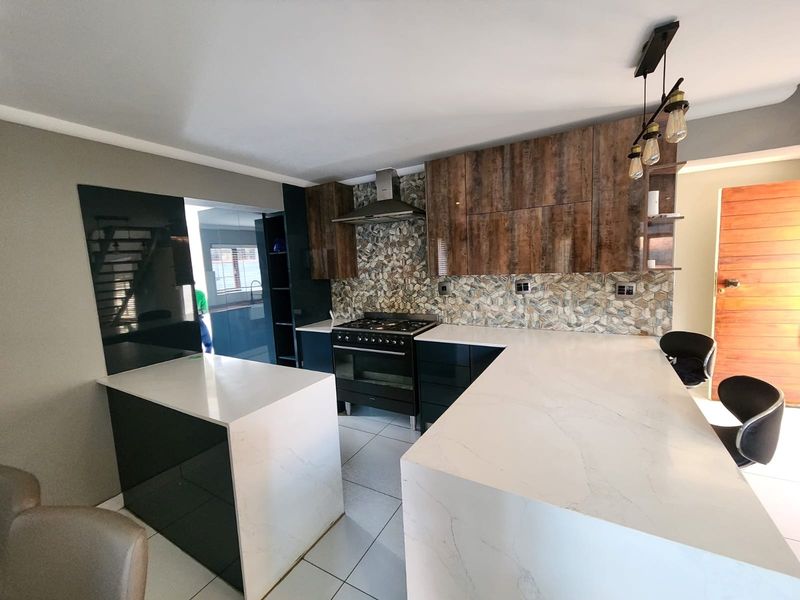 Modern kitchen featuring stone countertops, dark cabinetry, a gas stove with extractor fan, and a decorative mosaic tile backsplash.