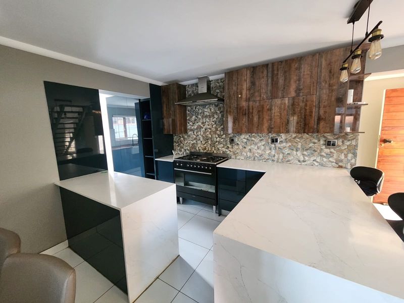 Modern kitchen featuring stone countertops, dark cabinetry, a gas stove with extractor fan, and a decorative tiled backsplash.
