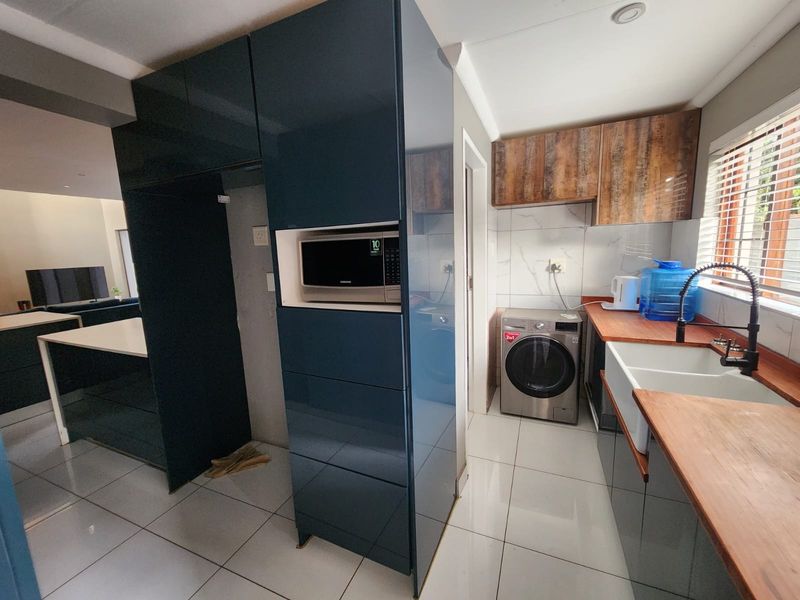 Modern kitchen featuring high-gloss dark cabinetry, wooden countertops, a farmhouse sink, and integrated microwave, with tiled flooring and a clean, contemporary aesthetic.