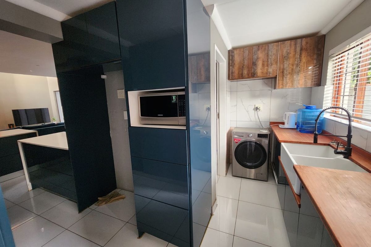 Modern kitchen featuring high-gloss dark cabinetry, wooden countertops, a farmhouse sink, and integrated microwave, with tiled flooring and a clean, contemporary aesthetic.