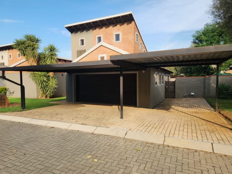 Front view of the property featuring a paved driveway, a double carport, and a brick-accented garage structure.
