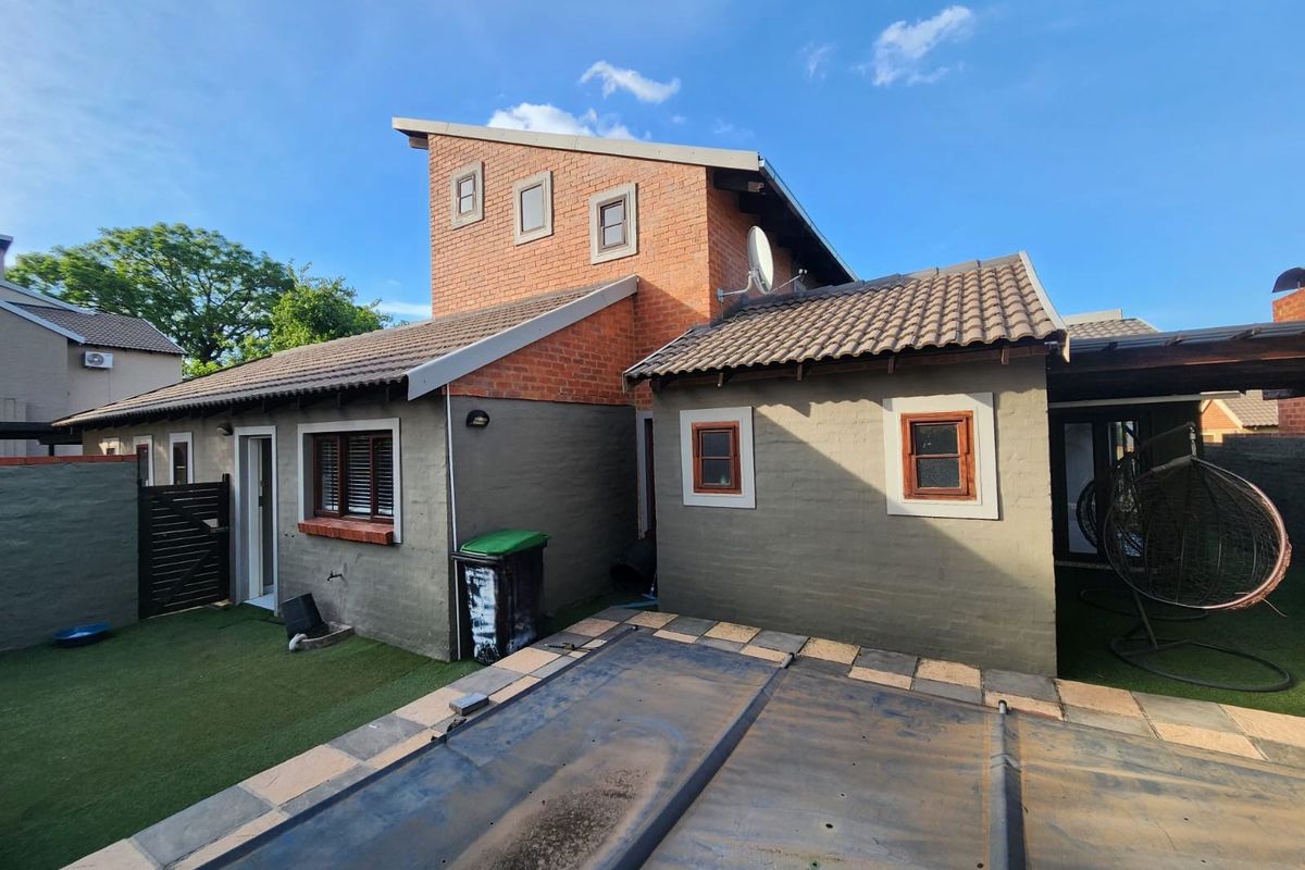 Rear view of the property featuring a multi-level brick and plastered facade, tiled roofing, and a swimming pool with a protective cover.