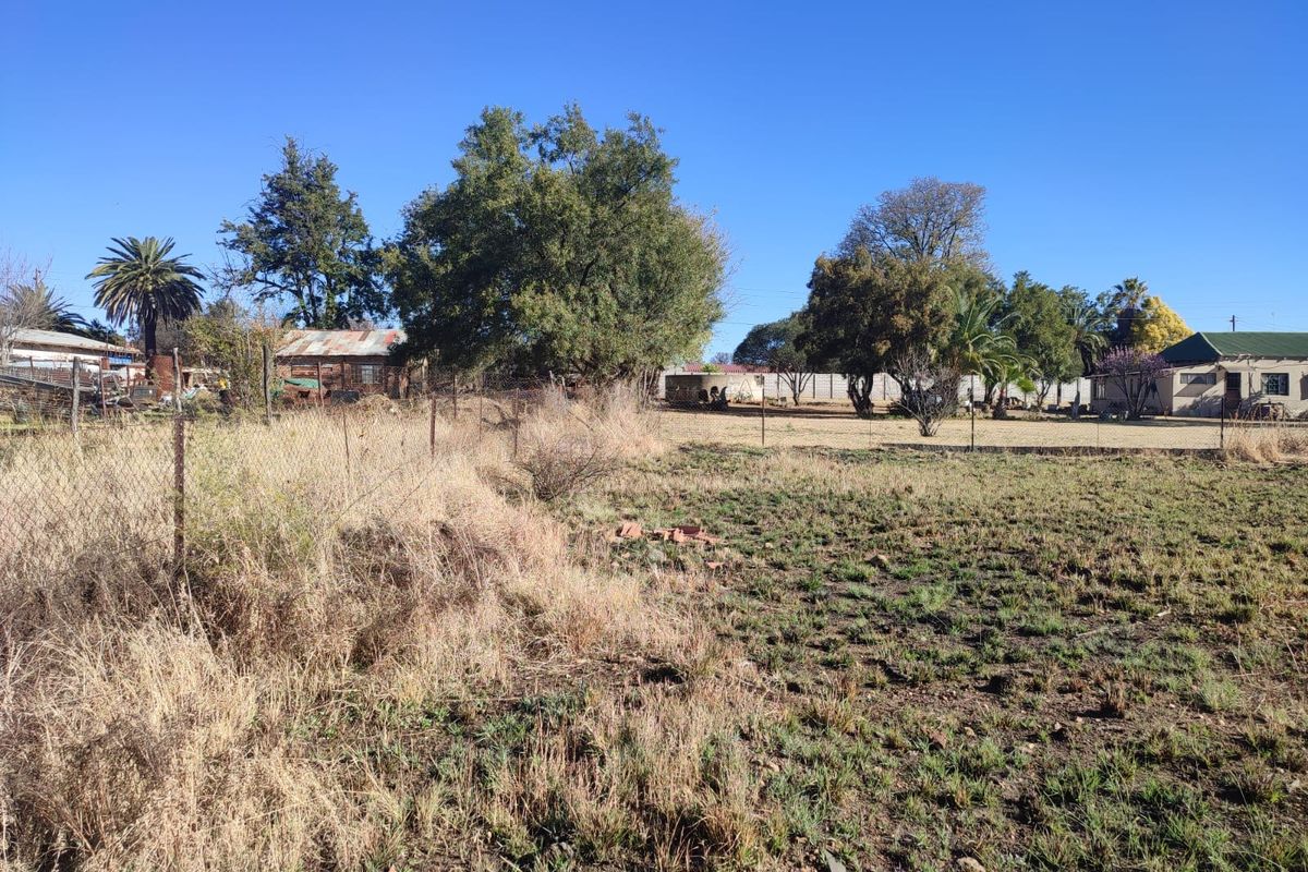 A view of a vacant residential plot featuring mature trees and perimeter wire fencing, offering potential for future development or landscaping.