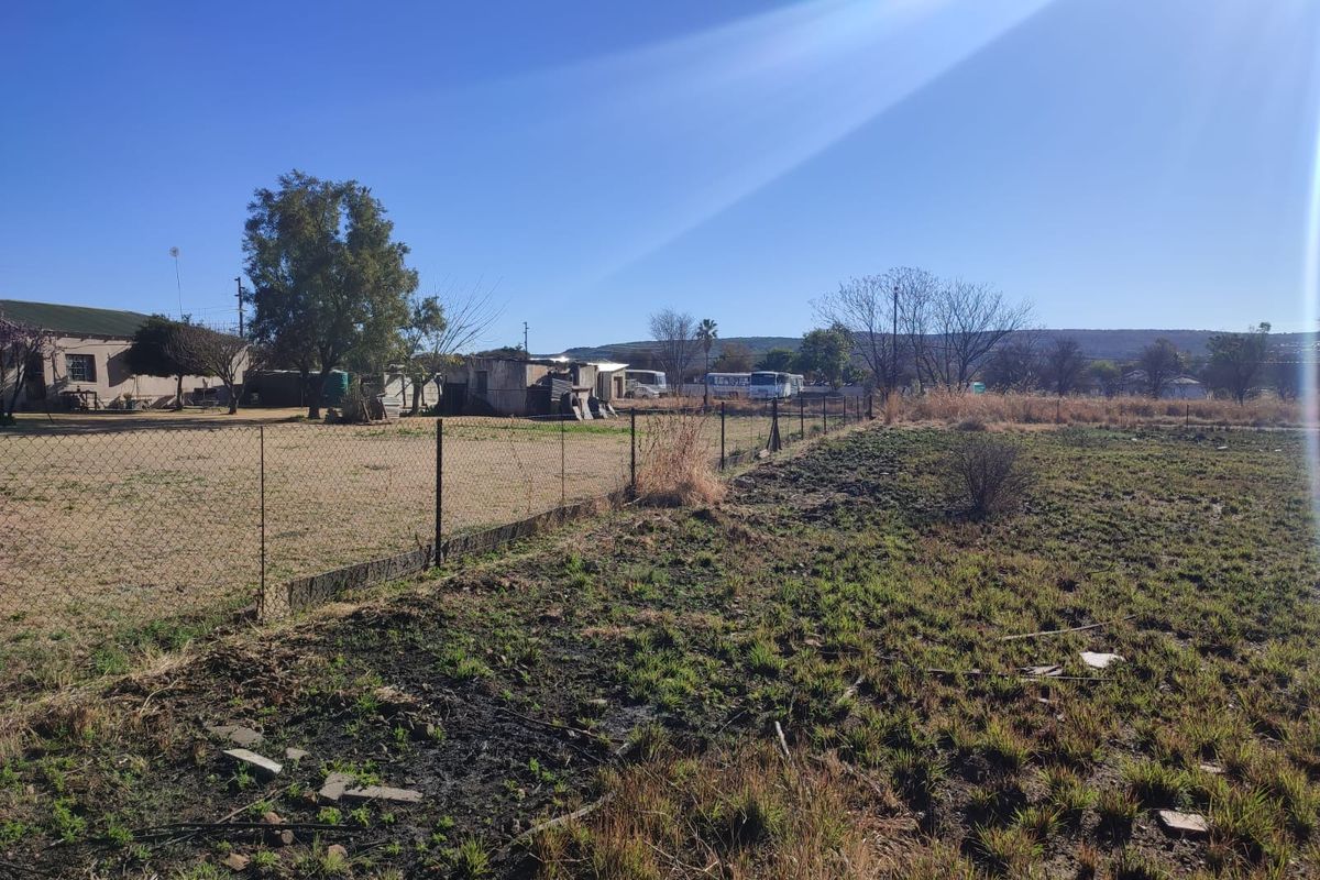 A view of a vacant residential plot featuring wire mesh fencing and open, undeveloped land with natural vegetation.