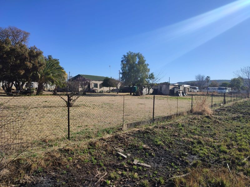 A view of a vacant residential plot featuring wire mesh fencing, mature trees, and level ground, suitable for future development.