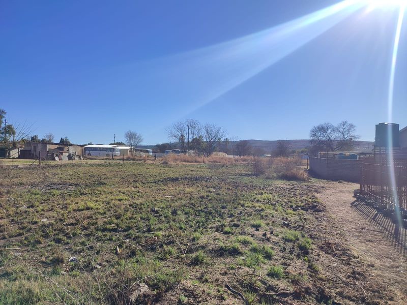 A vacant residential plot featuring perimeter fencing and a water storage tank, offering a clear space for future development.