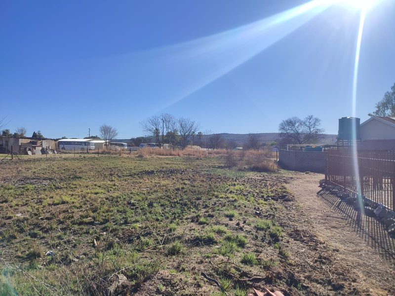 A vacant residential plot featuring perimeter fencing and a water storage tank, offering a clear view of the surrounding landscape.