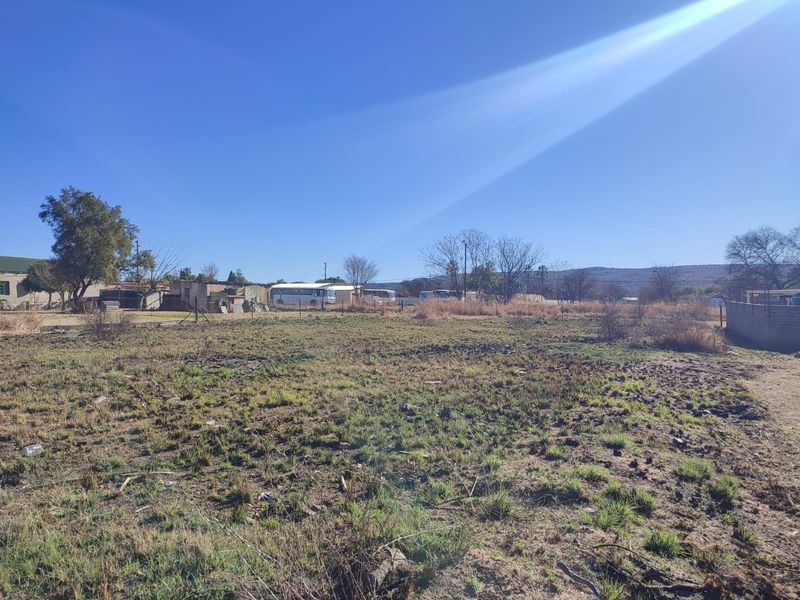 A view of an undeveloped residential plot of land featuring natural vegetation and perimeter wire fencing.