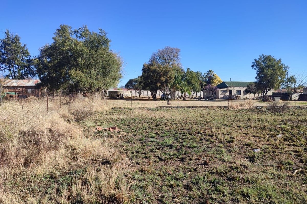 A view of a large, undeveloped residential plot featuring mature trees, wire fencing, and a water tank on the property.