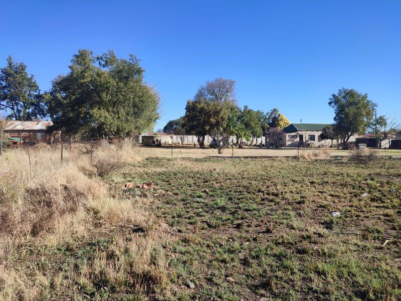 A view of a large, undeveloped residential plot featuring mature trees, wire fencing, and a water tank on the property.