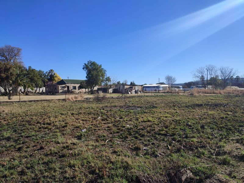 A view of a vacant residential plot featuring cleared land and perimeter wire fencing under a clear blue sky.