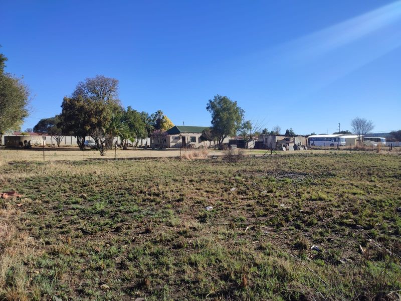 A wide-angle view of a vacant residential plot featuring level ground, perimeter fencing, and mature trees, offering potential for future development.