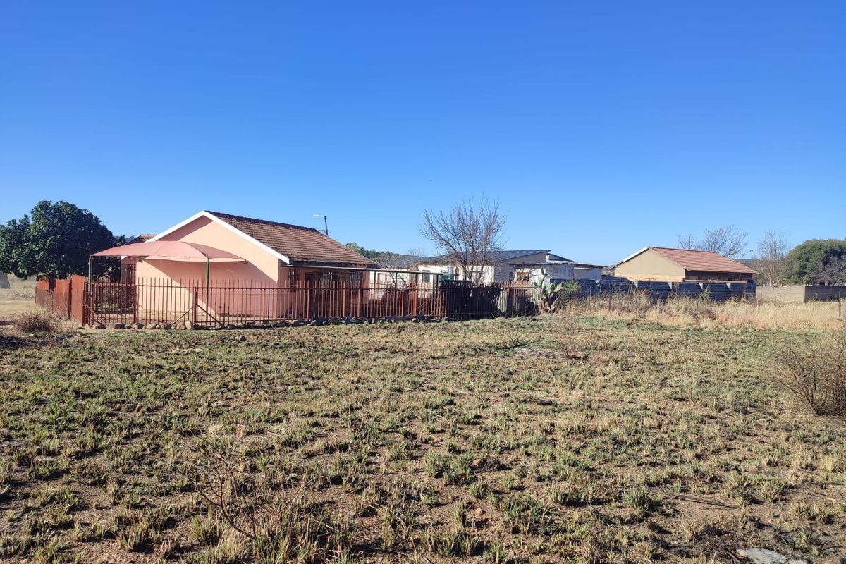 View of the rear exterior of the residential property featuring a tiled roof, covered patio area, and metal perimeter fencing on a large plot.