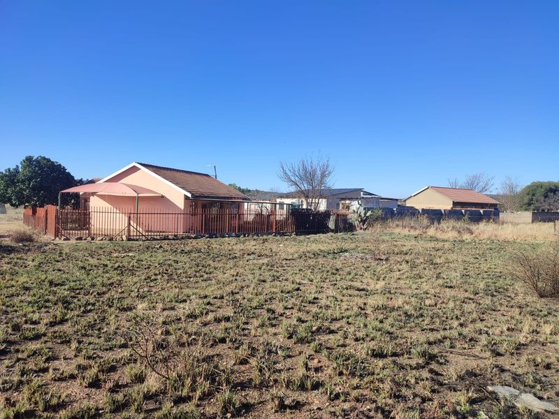 View of the rear exterior of the residential property featuring a tiled roof, covered patio area, and metal perimeter fencing on a large plot.
