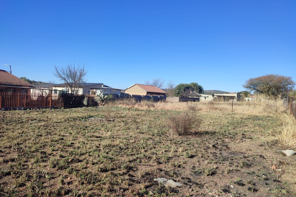 A vacant residential plot featuring natural ground cover and perimeter fencing, situated in an established neighborhood setting.