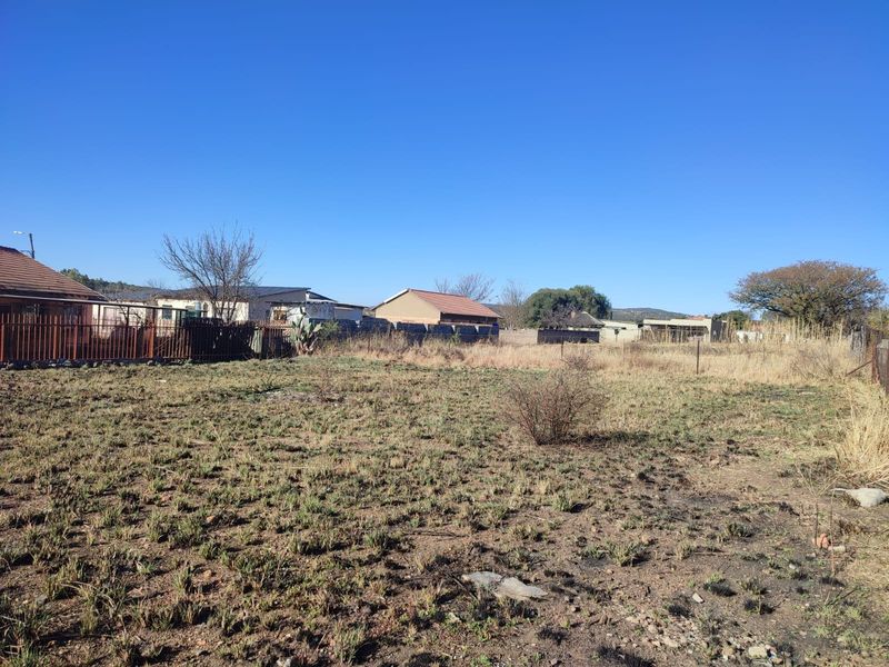 A vacant residential plot featuring natural ground cover and perimeter fencing, situated in an established neighborhood setting.