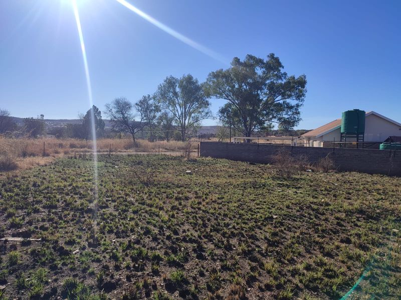 A vacant residential plot featuring a perimeter brick wall, wire fencing, and an existing water storage tank on the property.