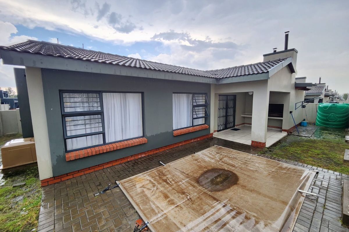 Rear exterior view of the townhouse featuring a paved patio area, built-in braai, and a covered pool.