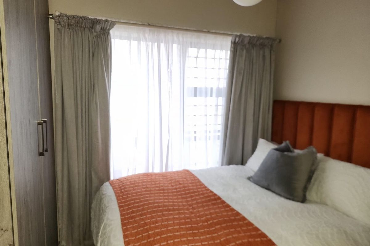 A cozy bedroom featuring a built-in wardrobe and natural light through a window with curtains.
