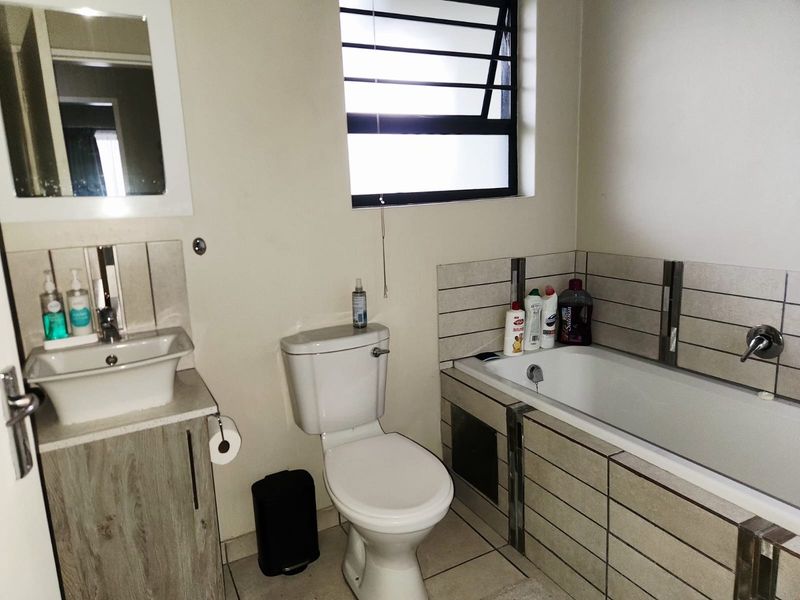 A functional bathroom featuring a vanity with basin, a standard toilet, and a tiled bathtub surround with a window for natural light.