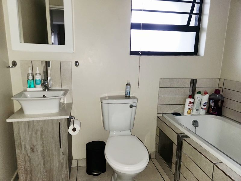 A functional bathroom featuring a vanity with a vessel sink, a standard toilet, and a bathtub with tiled surround and a louvre window.