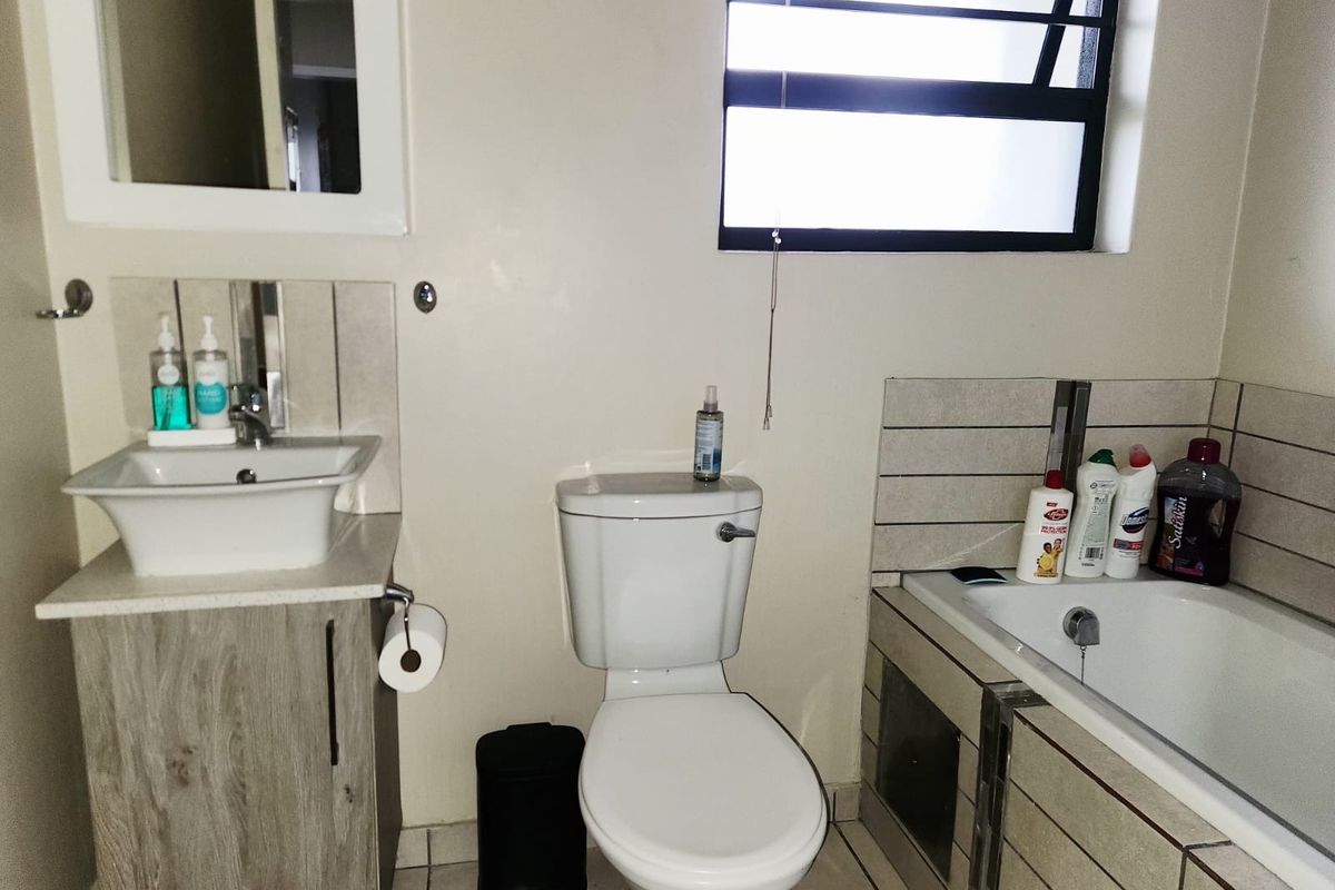 A functional bathroom featuring a vanity with a vessel sink, a standard toilet, and a bathtub with tiled surround and a louvre window.