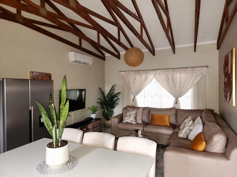 Open-plan living area featuring high vaulted ceilings with exposed timber trusses and a wall-mounted air conditioning unit.