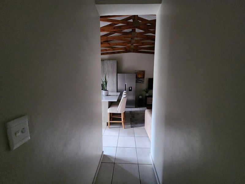 View through a hallway into an open-plan living and kitchen area featuring exposed timber roof trusses and tiled flooring.