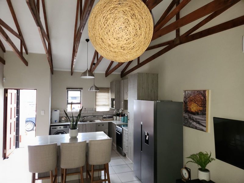 Open-plan kitchen and living area featuring high vaulted ceilings with exposed timber trusses, tiled flooring, and a functional kitchen layout with built-in cabinetry.