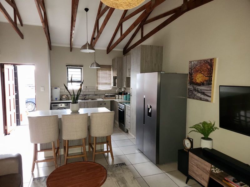 Open-plan living and kitchen area featuring high vaulted ceilings with exposed timber trusses, modern cabinetry, and tiled flooring throughout.