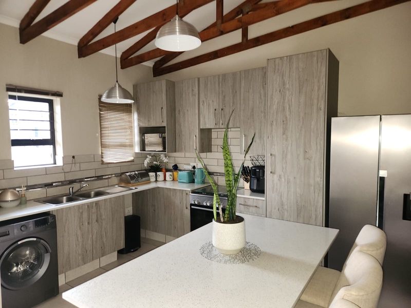 Modern kitchen featuring light wood-grain cabinetry, stone countertops, exposed timber rafters, and integrated appliances, creating a bright and functional culinary space.