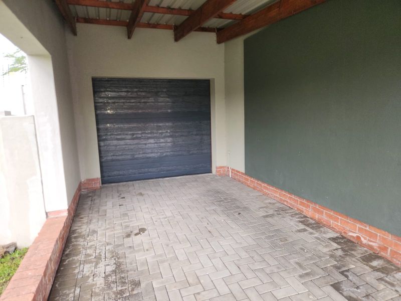 A covered garage area featuring paved flooring, exposed timber rafters, and a secure garage door.