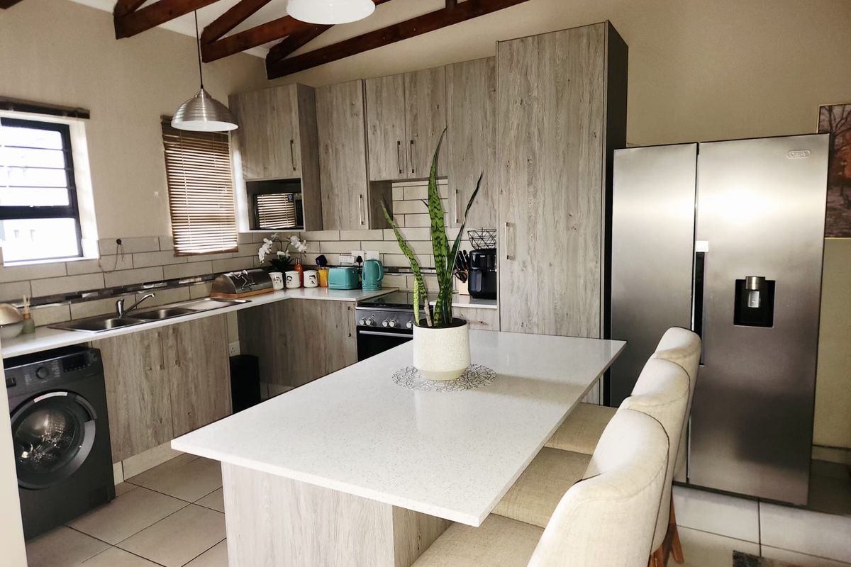 Modern kitchen featuring wood-look cabinetry, stone countertops, a central island, and exposed timber ceiling beams, creating a warm and functional culinary space.