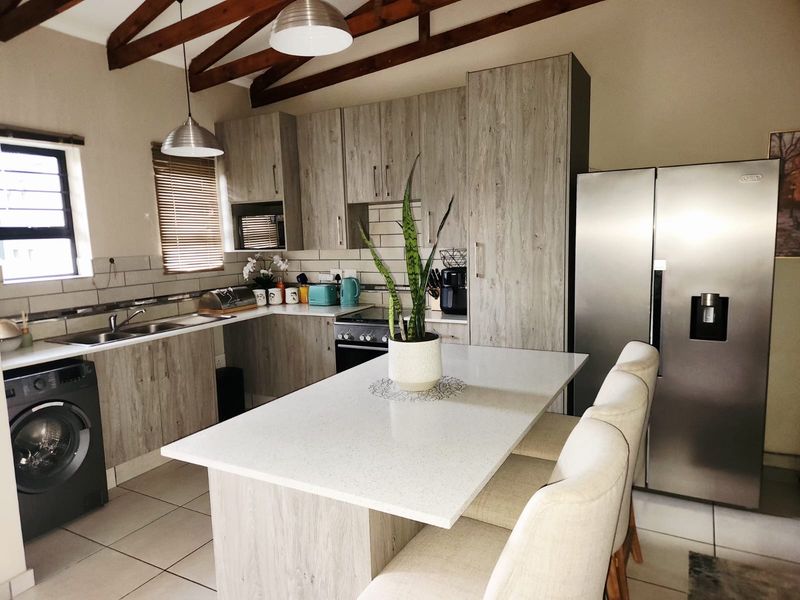 Modern kitchen featuring wood-look cabinetry, stone countertops, a central island, and exposed timber ceiling beams, creating a warm and functional culinary space.