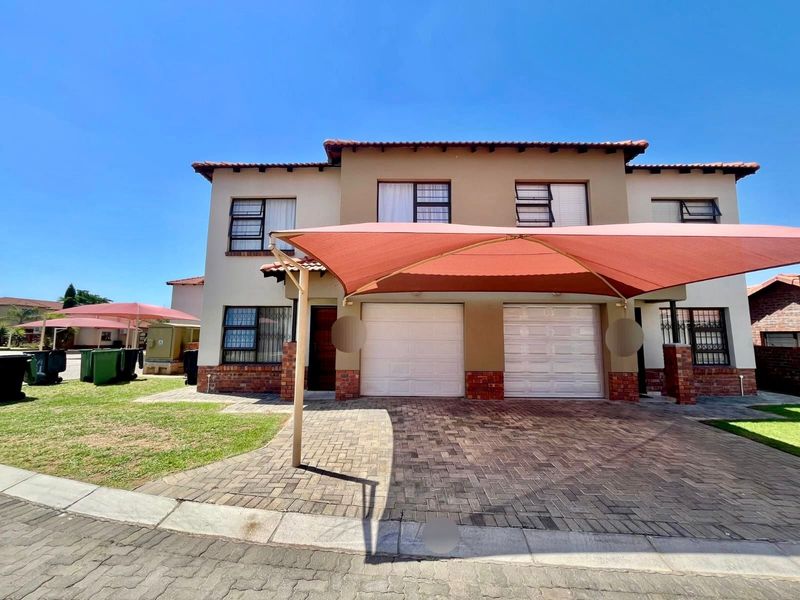 Front elevation of a double-story townhouse featuring a paved driveway, double garage, and a large shade sail covering the parking area.