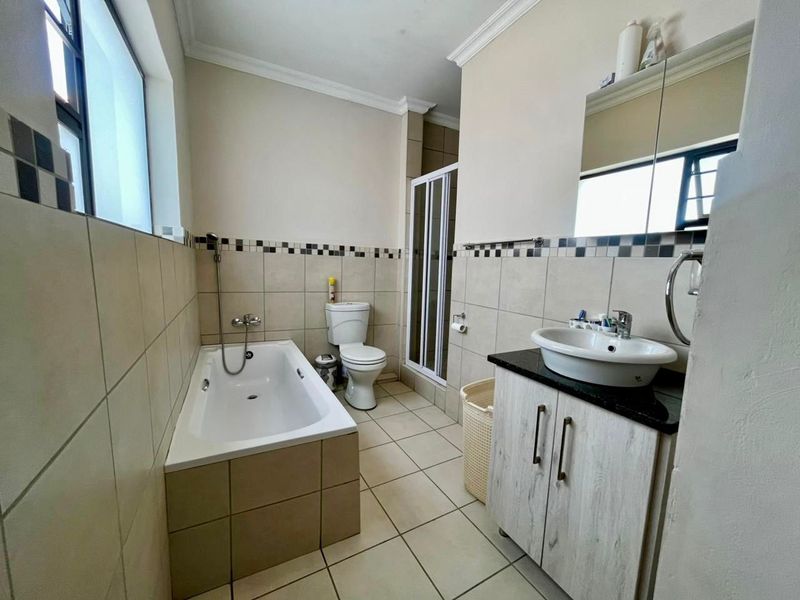 A functional bathroom featuring a bathtub, separate shower enclosure, vessel sink with vanity cabinet, and neutral wall and floor tiling.