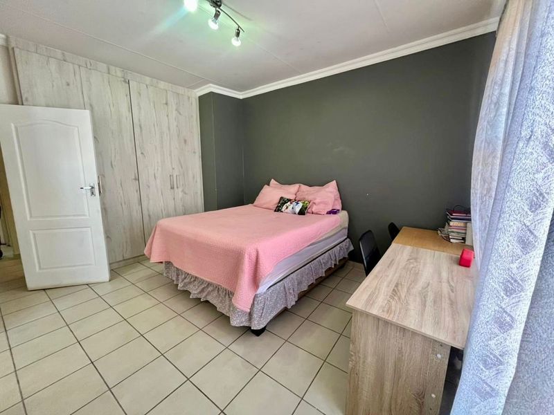 A bedroom featuring tiled flooring, built-in cupboards, and a dark accent wall, providing a functional living space.