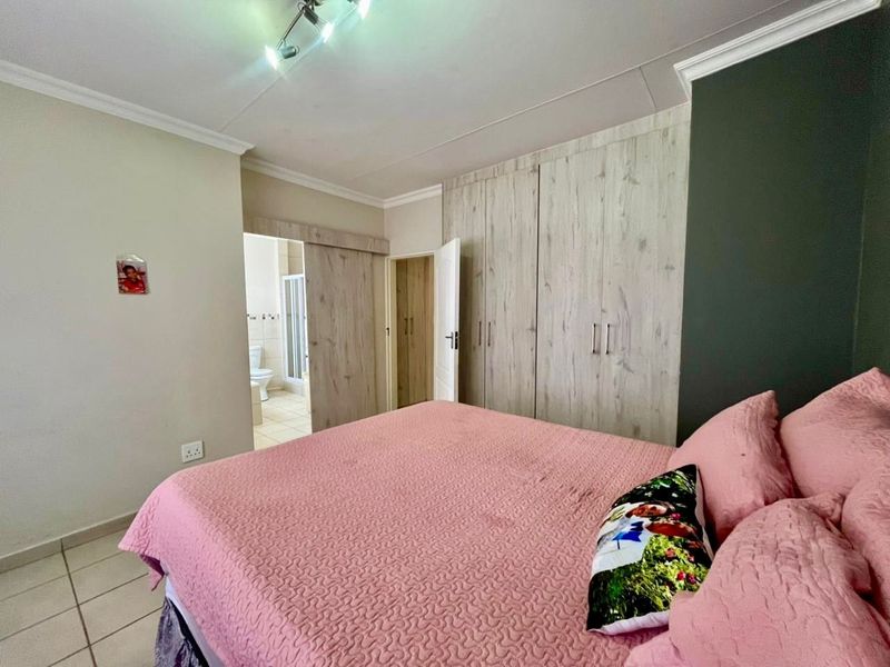 A well-maintained bedroom featuring built-in wooden cupboards, tiled flooring, and direct access to an en-suite bathroom.