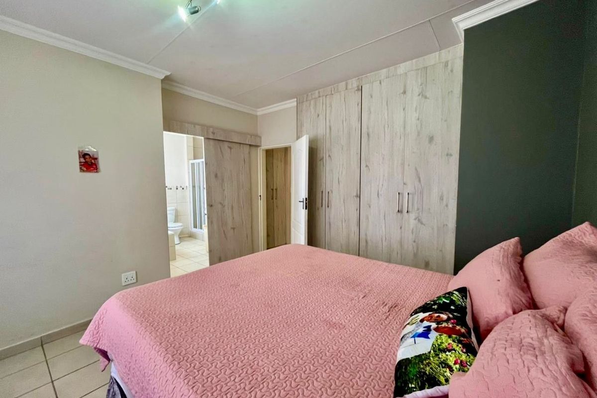 A well-maintained bedroom featuring built-in wooden cupboards, tiled flooring, and direct access to an en-suite bathroom.