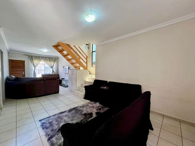 Open plan living area featuring tiled flooring and a wooden staircase with a handrail, providing access to the upper level of the townhouse.