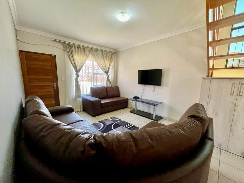 A functional living room featuring tiled flooring, a wooden staircase, and built-in storage, providing a practical layout for daily living.