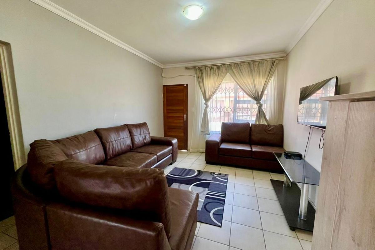 A functional living room featuring tiled flooring, ceiling cornicing, and secure window bars, providing a comfortable and practical space for relaxation.