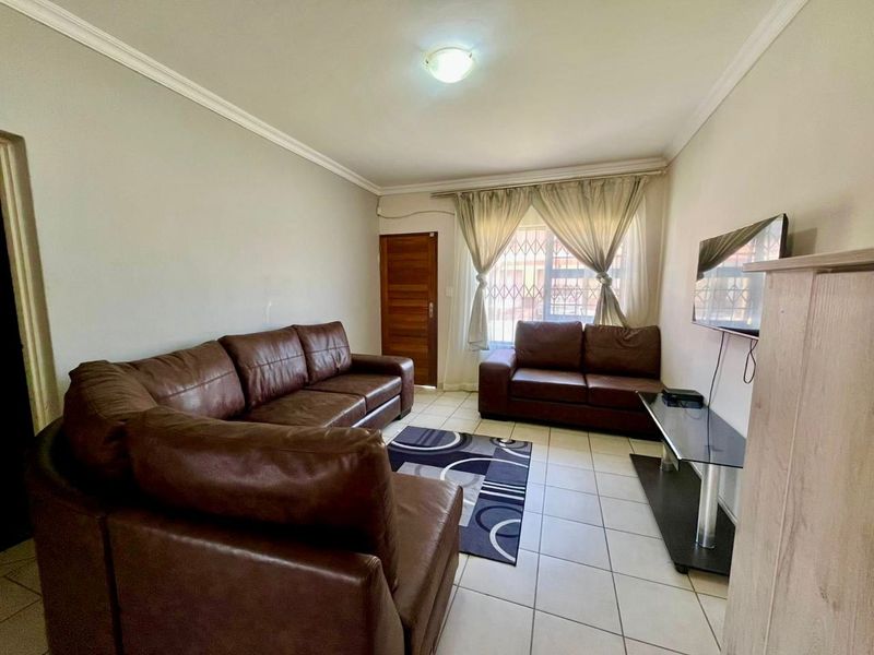 A functional living room featuring tiled flooring, ceiling cornicing, and secure window bars, providing a comfortable and practical space for relaxation.