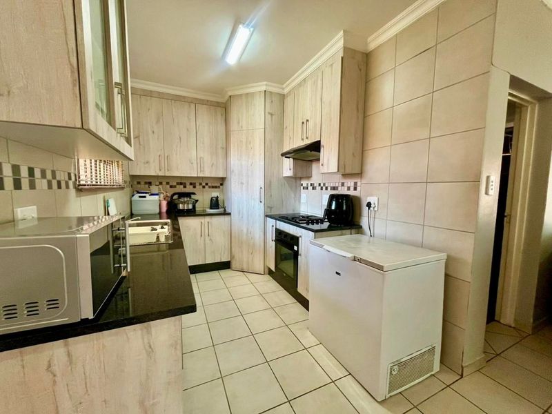 A functional kitchen featuring light wood-finish cabinetry, granite countertops, a built-in oven with gas hob, and tiled flooring throughout.