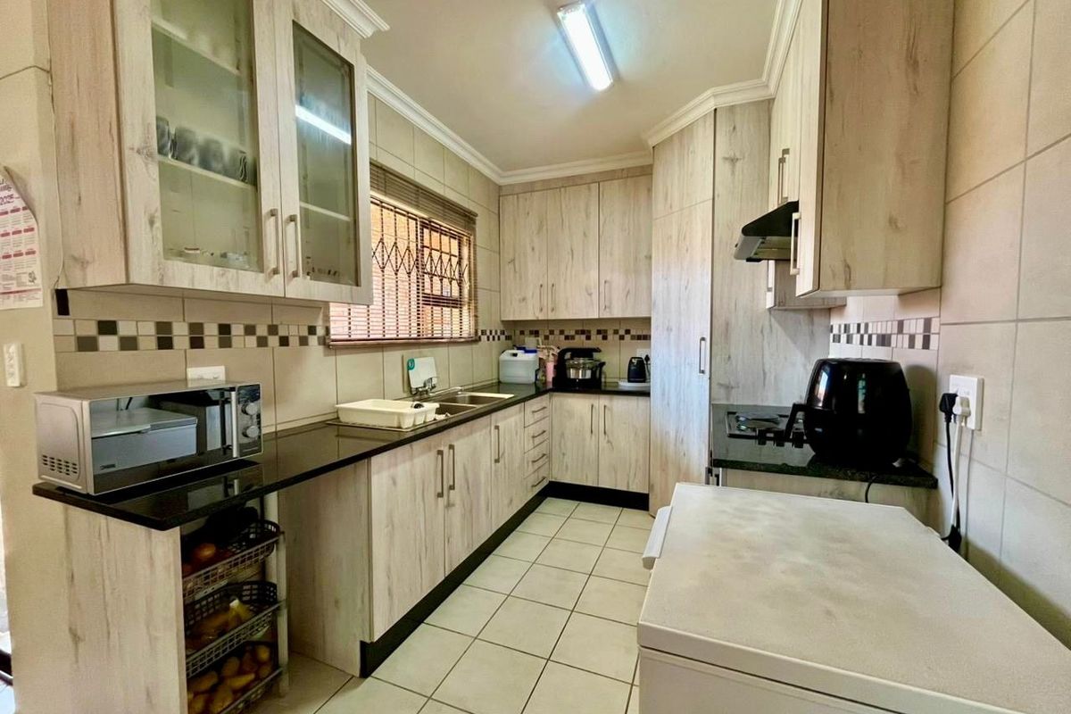 Functional kitchen featuring light wood-look cabinetry, dark granite countertops, tiled backsplash, and ample storage space with integrated extractor fan.