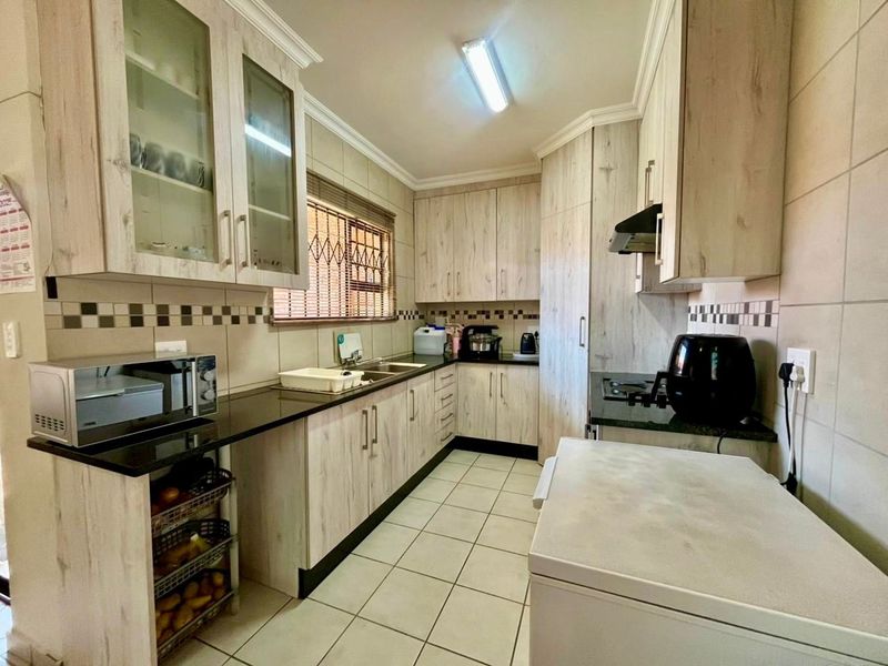 Functional kitchen featuring light wood-look cabinetry, dark granite countertops, tiled backsplash, and ample storage space with integrated extractor fan.
